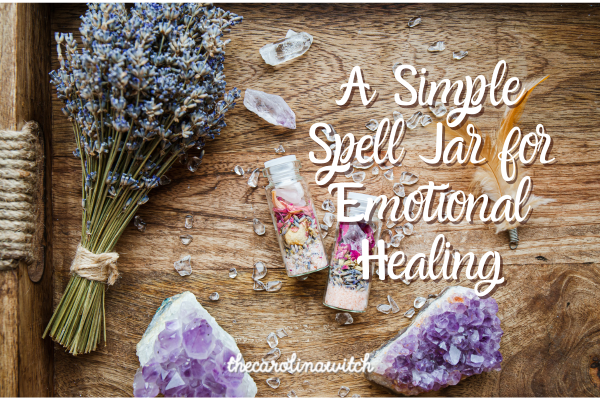 A simple spell jar for emotional healing blog post title with a picture of a small spell jar sitting on a wooden table surrounded by amethyst crystals and dried lavender.